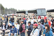 A group of people sitting and standing in front of 3 tour buses