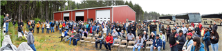 A group of people outside a barn listening to a speaker