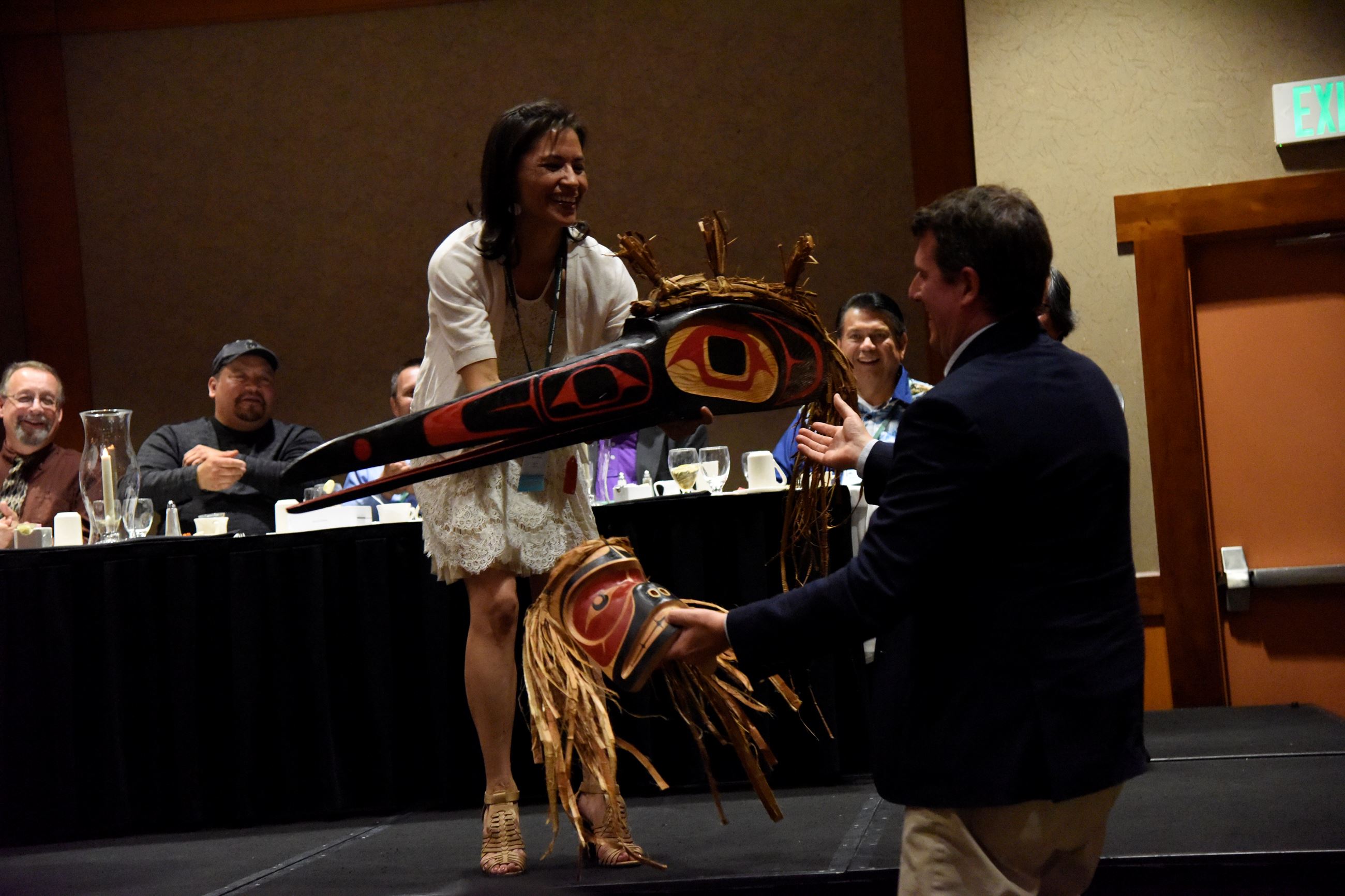 A woman hands a man a mask and a ceremonial object