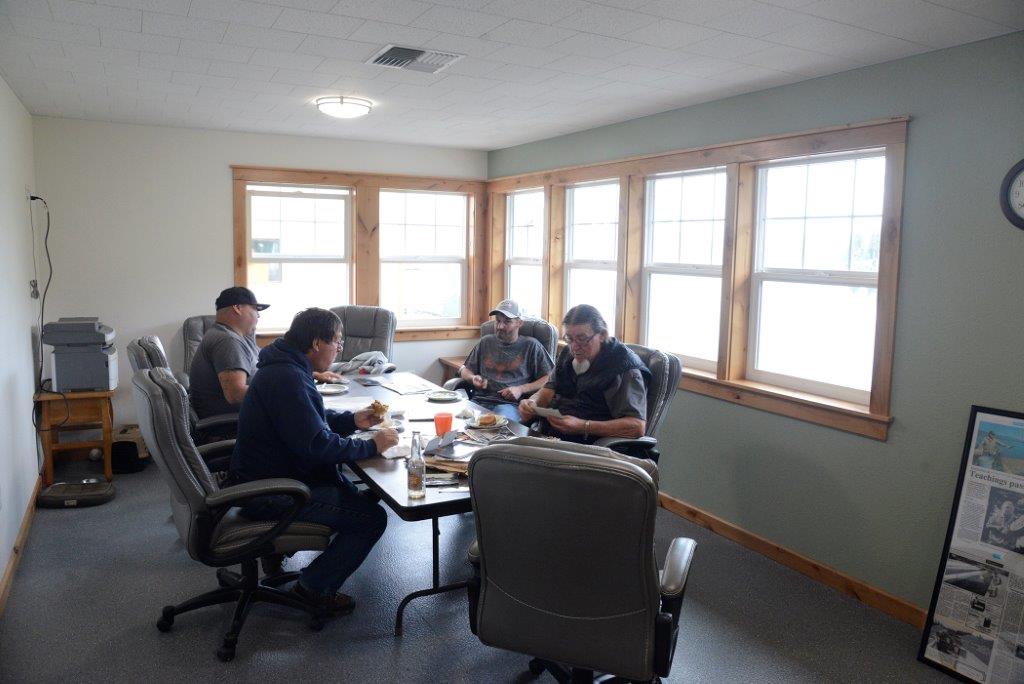 4 men sit in a small room around a table in office chairs